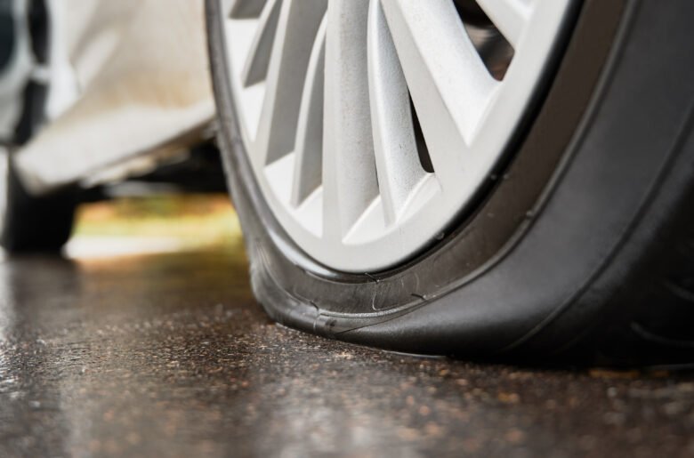 Stopped white car with punctured tire on roadside. Stopped white car with punctured tire on roadside.